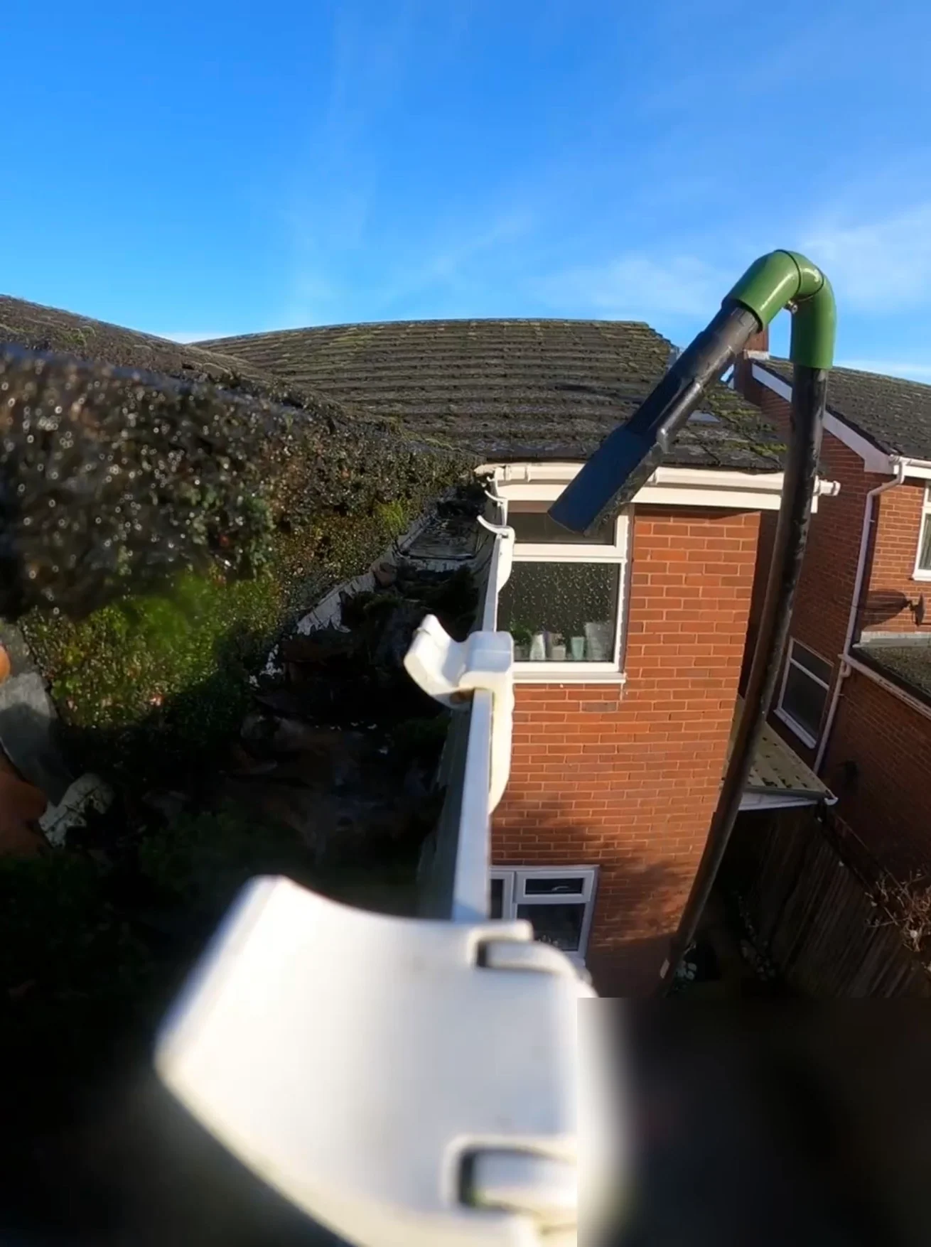 Roof edge gutter clogged with moss and debris before vacuum clearing